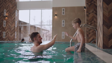 joyful-little-boy-is-playing-with-dad-in-swimming-pool-rest-in-family-wellness-center-in-weekend